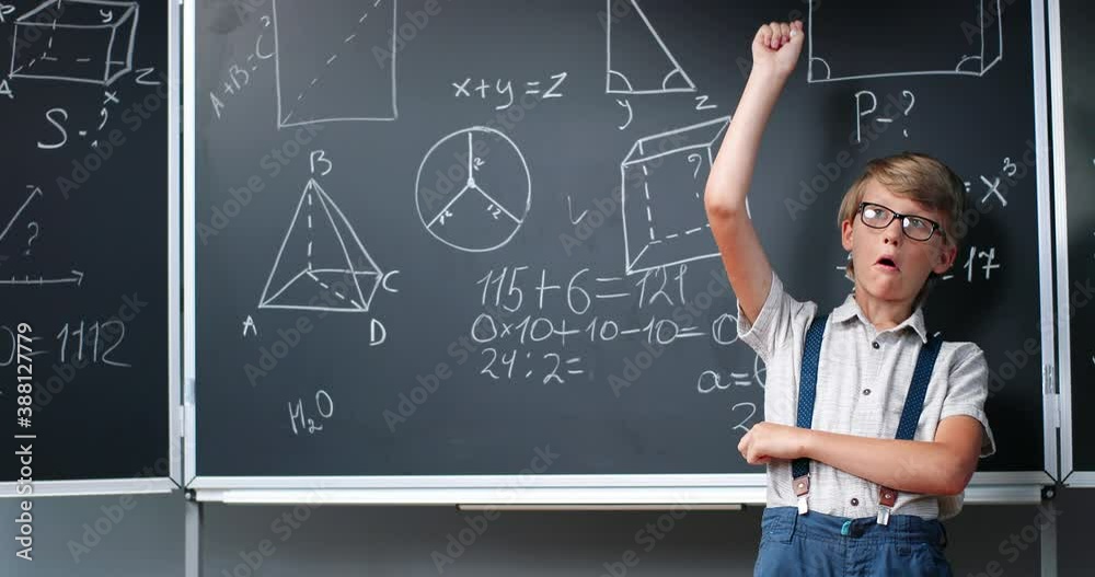 Portrait of Caucasian small teen boy standing at blackboard in classroom and deciding math formulas and equations. Teenage smart schoolboy studying mathematics at chalkboard. Algebra or geometry. Portrait of Caucasian small teen boy standing at blackboard in classroom and deciding math formulas and equations. Teenage smart schoolboy studying mathematics at chalkboard. Algebra or geometry.
