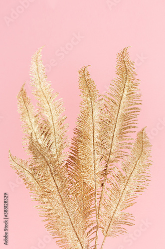 Luxury golden fern branch on soft light pastel pink background, vertical.