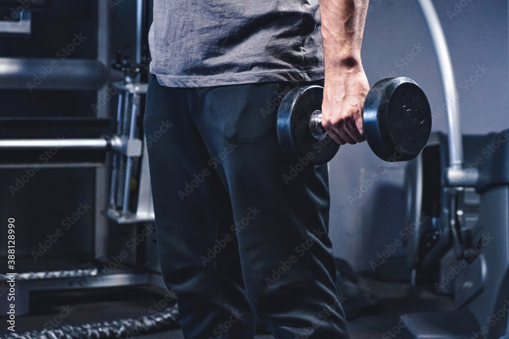 Naklejka premium Athletic young man workout in gym with dumbbells