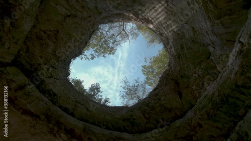 cloudy sky through opening gap in cave ceiling. Camera look vertical up, pan move.
