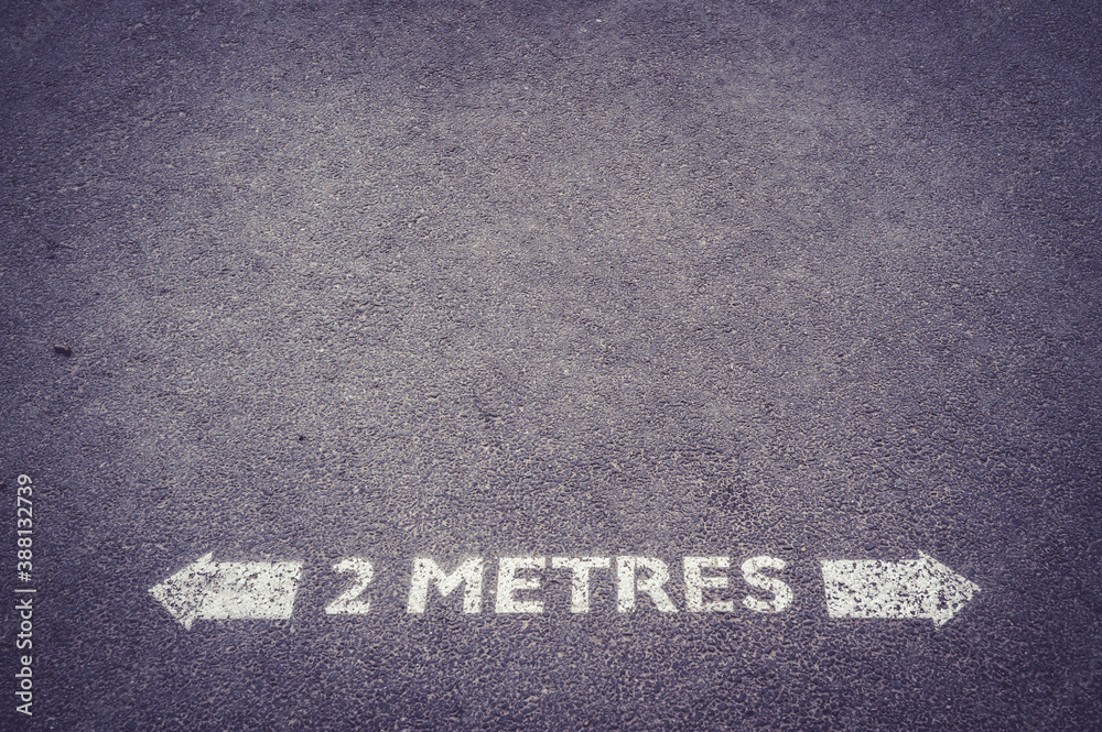 Fototapeta premium Social distancing road painted sign recommending staying 2 metres apart