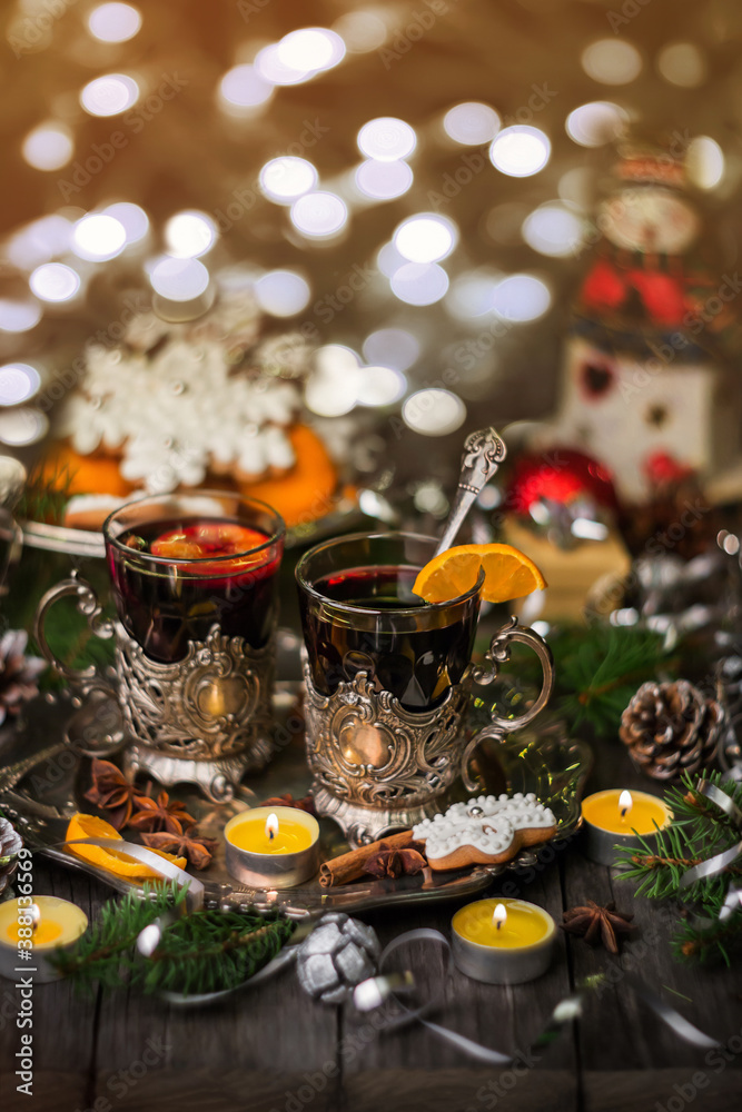 Two glasses of mulled wine in cup holders, with cinnamon and anise on a wooden background with fir branches and candles. Winter Christmas still life, beautiful bokeh, postcard in vintage style.