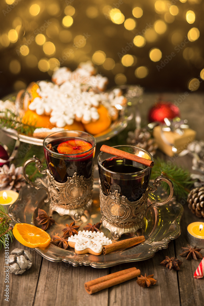 Two glasses of mulled wine in cup holders, with cinnamon and anise on a wooden background with fir branches and candles. Winter Christmas still life, beautiful bokeh, postcard in vintage style.