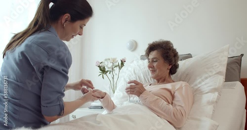 Nurse Administering Medications to Female Senior Patient. Cheerful Home Caregiver Giving Pills to Elderly Female Patient Lying in Bed.