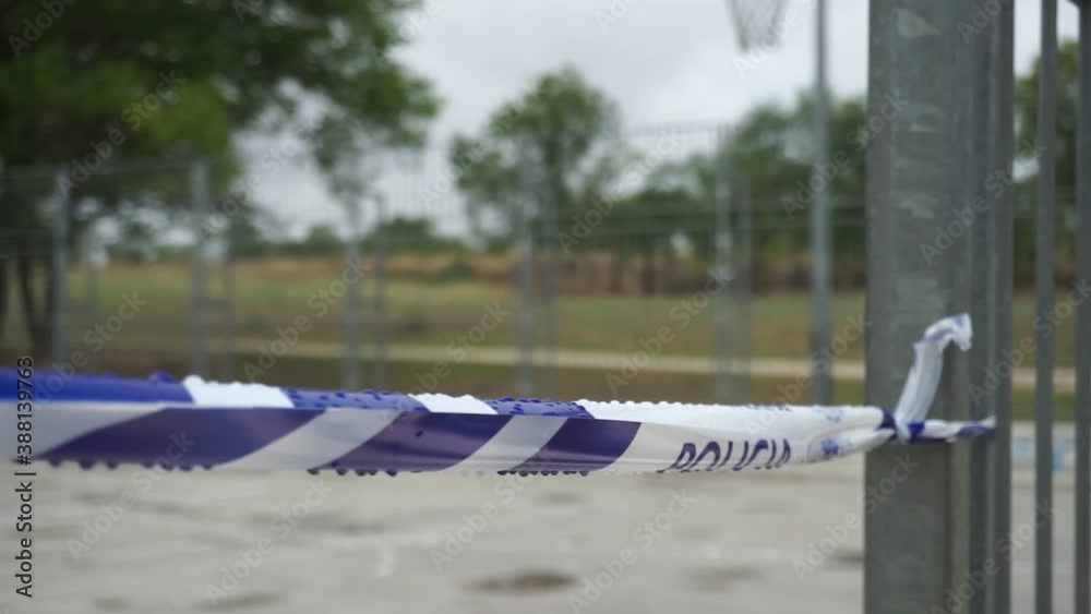 Police tape with 'policia' text tied to fence on basketball court, pull back shot Police tape with 'policia' text tied to fence on basketball court, pull back shot