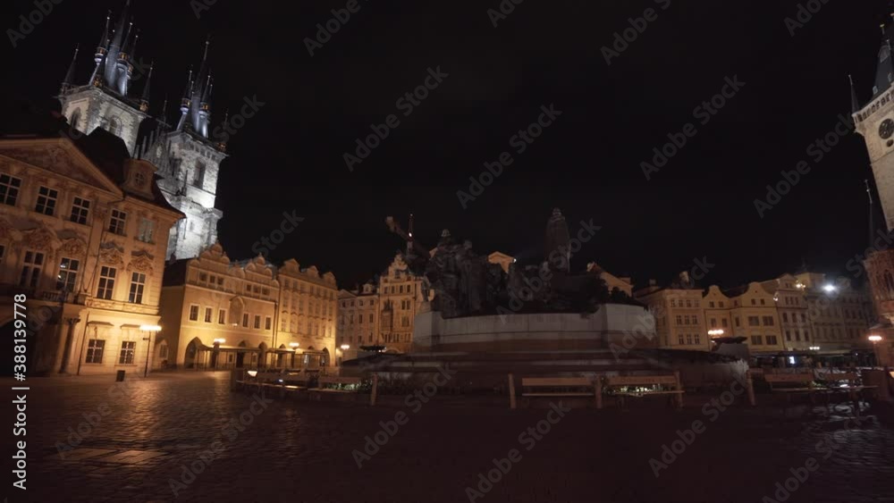 The monument of Jan Hus on the Old Town Square in the historical center of Prague,Czechia,at night,empty due to a Covid-19 lockdown,a gothic cathedral and the Astronomical tower,Orloj,behind,pan. The monument of Jan Hus on the Old Town Square in the historical center of Prague,Czechia,at night,empty due to a Covid-19 lockdown,a gothic cathedral and the Astronomical tower,Orloj,behind,pan.