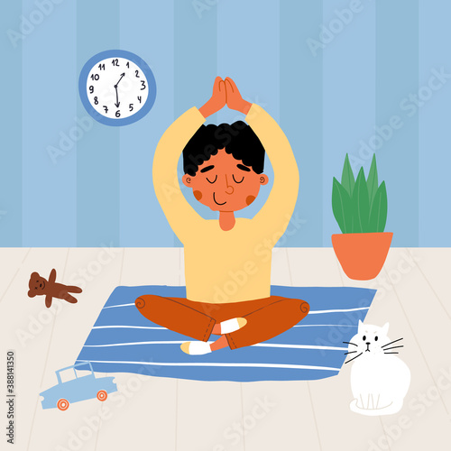 Cute meditating or doing yoga exercise Indian kid in lotus pose with his hands up above his head, amazed cat nearby.