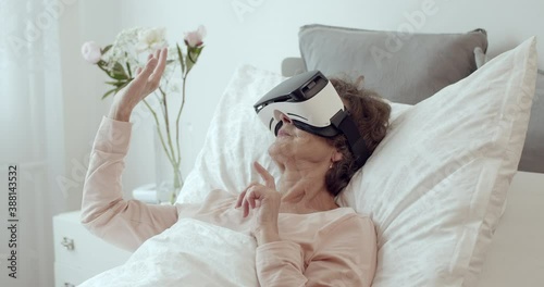 Elderly Patient Lying in Hospital Bed Doing Therapy Via VR Technology. Senior Woman Receiving Therapy Using Virtual Reality Headset.