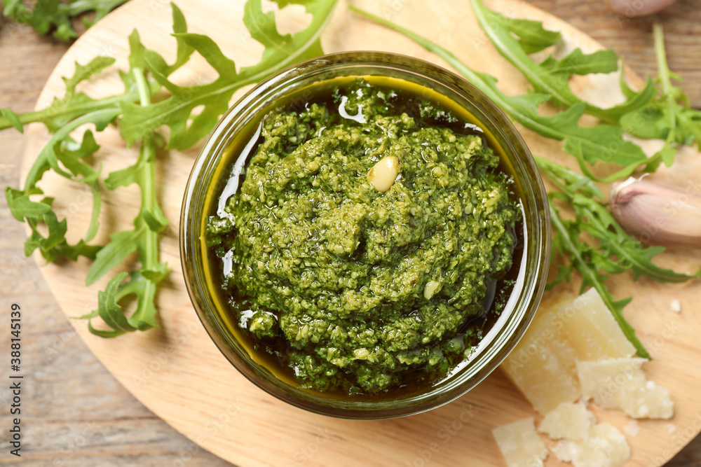 Bowl of tasty arugula pesto and ingredients on wooden board, flat lay Bowl of tasty arugula pesto and ingredients on wooden board, flat lay