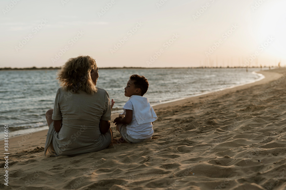 Grandmother and grandson talking with each other at beach during sunset Grandmother and grandson talking with each other at beach during sunset