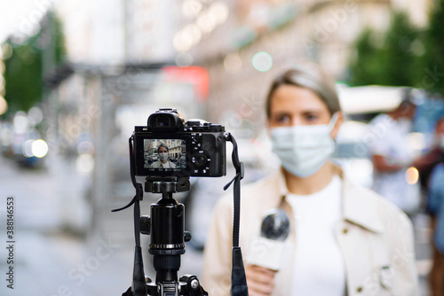 Female journalist wearing mask filming with camera in city photo