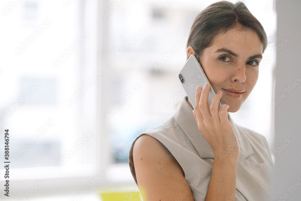 Beautiful businesswoman talking on mobile phone while standing at office Beautiful businesswoman talking on mobile phone while standing at office