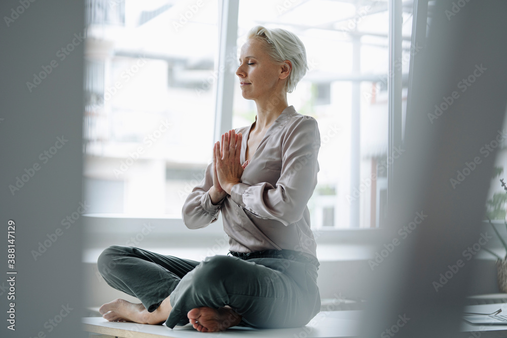 Businesswoman with eyes closed meditating while sitting against window in loft office Businesswoman with eyes closed meditating while sitting against window in loft office