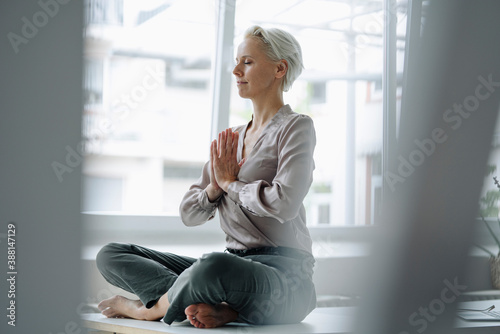 Businesswoman with eyes closed meditating while sitting against window in loft office photo