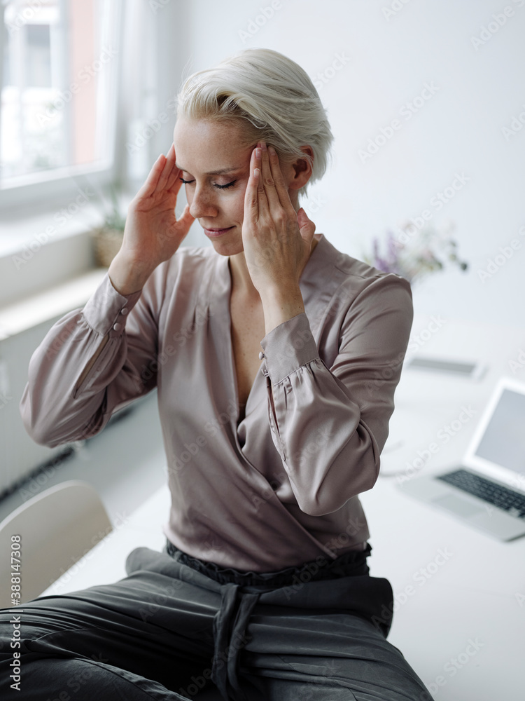 Businesswoman with head in hands meditating sitting on desk at loft office Businesswoman with head in hands meditating sitting on desk at loft office