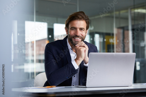 Smiling businessman using laptop while sitting on chair in office photo