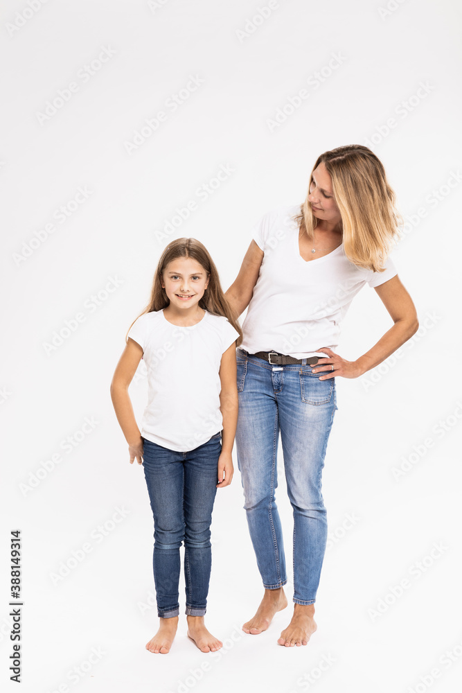 Mother with hand on hip looking at daughter while standing against white background Mother with hand on hip looking at daughter while standing against white background