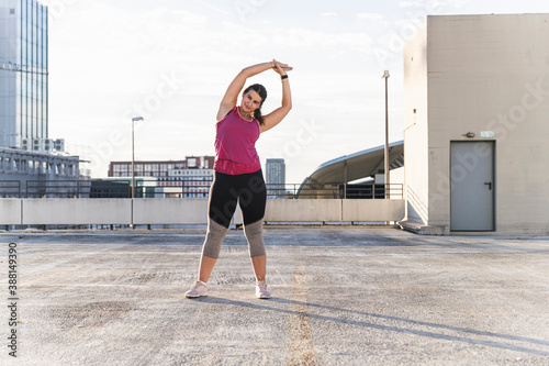 Young woman with arms raised exercising while standing on terrace against sky photo