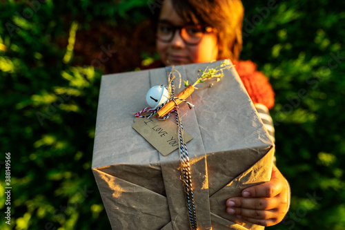 Close-up of boy holding Christmas present while standing against plants in yard photo