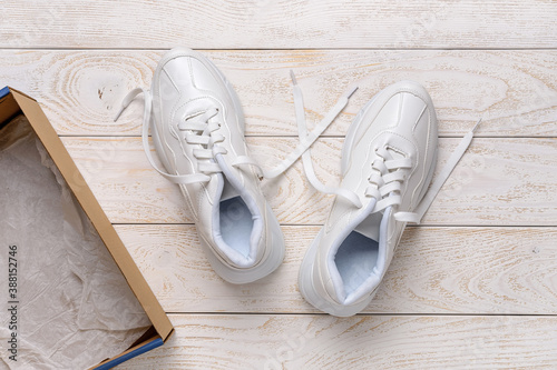 Pair of white chunky sole sneakers near brown cardboard box on the white wood floor. Open box with new comfortable shoes for active lifestyle, fitness and sports.