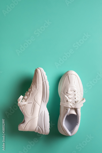 One sneaker stands and the other lies on its side on a green blue background. New white chunky sole shoes for active lifestyle, fitness and sports. Vertical frame with copy space.