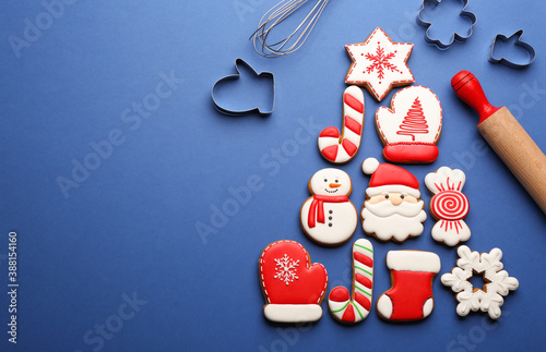 Kitchen utensils near Christmas tree shape made of delicious gingerbread cookies on blue background, flat lay. Space for text
