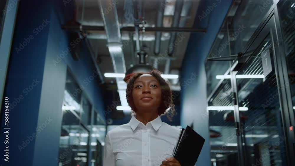 Smiling afro woman waving hand in corridor. Friendly businesswoman saying hi