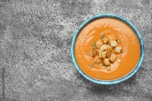 Tasty creamy pumpkin soup with croutons and seeds in bowl on grey table, top view. Space for text