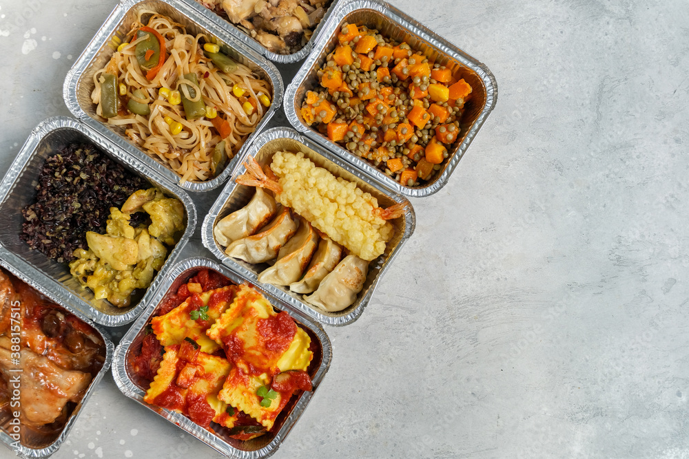 Food delivery. Different aluminium lunch box with ravioli, curry chicken  rice, gyoza tempura, noodles vegetables, lentils with pumpkin . airlines meals and snacks. takeaway takeout coronavirus food