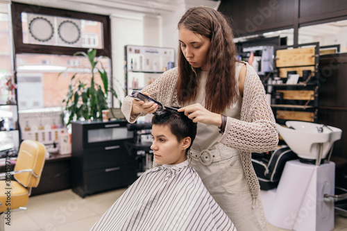 Female hairstylist trimming hair of androgynous client in salon photo