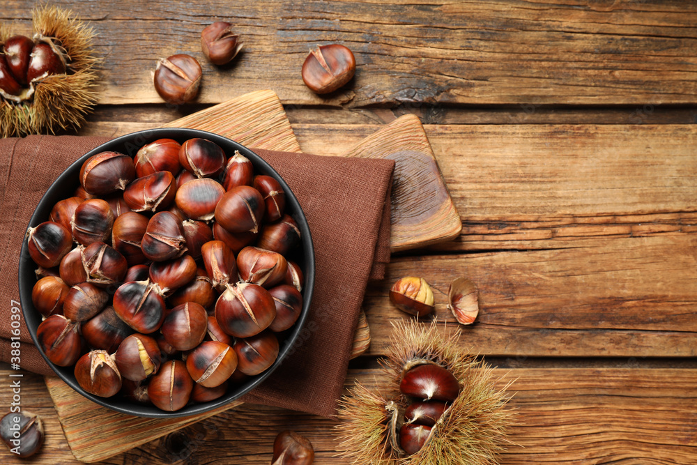 Delicious roasted edible chestnuts on wooden table, flat lay. Space for text - obrazy, fototapety, plakaty 