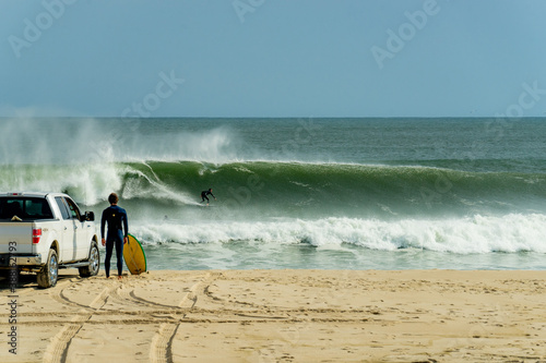 Photography A surfer charges down the face of a breaking wave while 2 people watch from shore