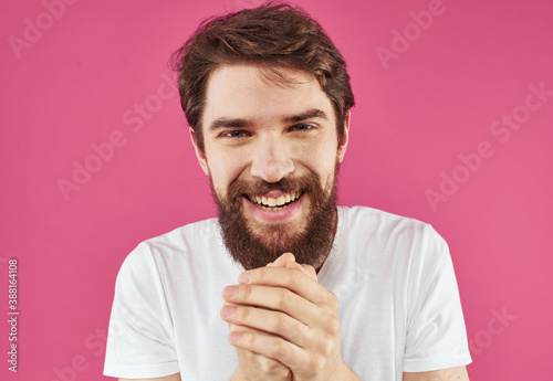 Portrait of a happy guy in a white T-shirt with a thick beard on a pink background