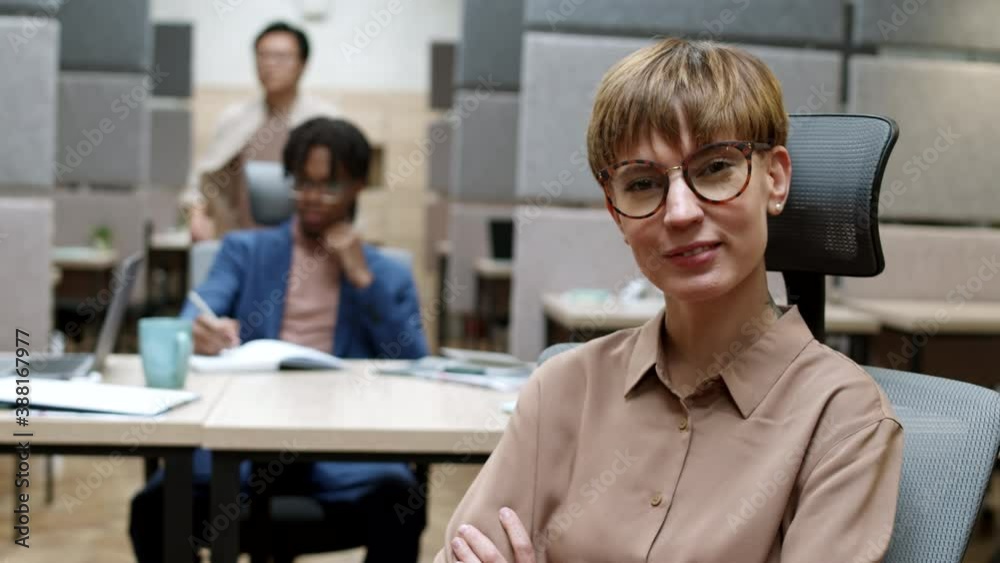 Medium shot of attractive Caucasian woman wearing fashionable clothes and eyeglasses sitting on office chair in modern coworking space, turning around and looking at camera Medium shot of attractive Caucasian woman wearing fashionable clothes and eyeglasses sitting on office chair in modern coworking space, turning around and looking at camera