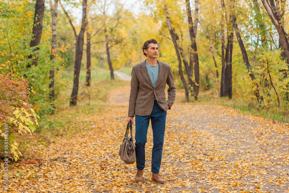 Tall handsome man with a bag on the autumn alley