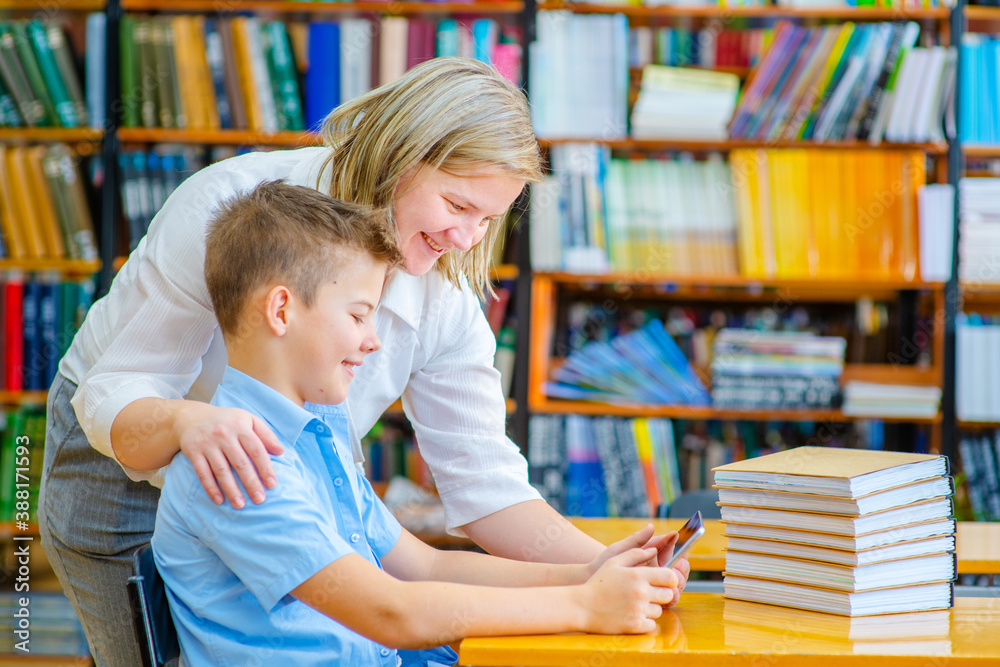 A teacher who comes up helps a boy sitting at a computer in the library. Tutoring in schools concept A teacher who comes up helps a boy sitting at a computer in the library. Tutoring in schools concept