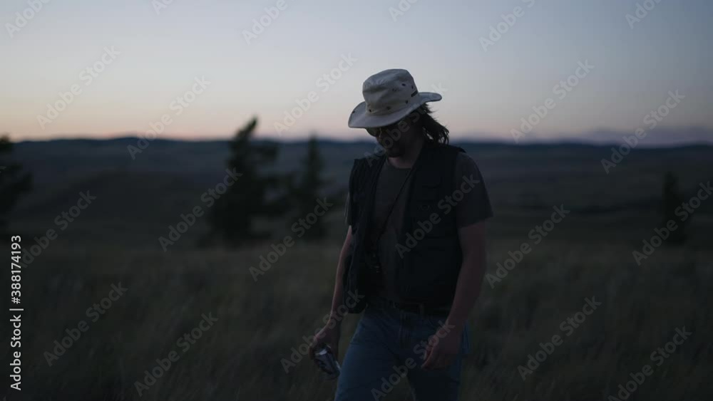 Man in hat walks through natural landscape holding can of beer or soda at dusk Man in hat walks through natural landscape holding can of beer or soda at dusk