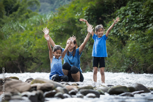 Asian mother and her daughters playing in the river together with fun and enjoy with nature.