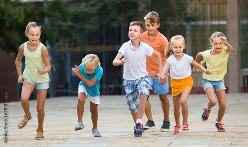 Group of friendly children in school age running together in town on summer