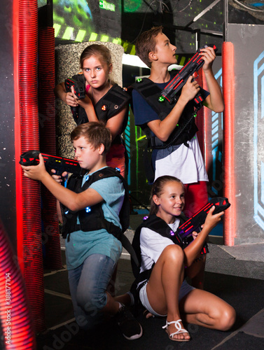 Cheerful teen girls and boys with laser pistols posing together in dark laser tag labyrinth..
