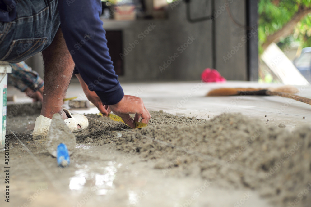 Selective focus on leg and hands of worker mearsuring the floor during installation the floor tiles in the ouse under construction Selective focus on leg and hands of worker mearsuring the floor during installation the floor tiles in the ouse under construction
