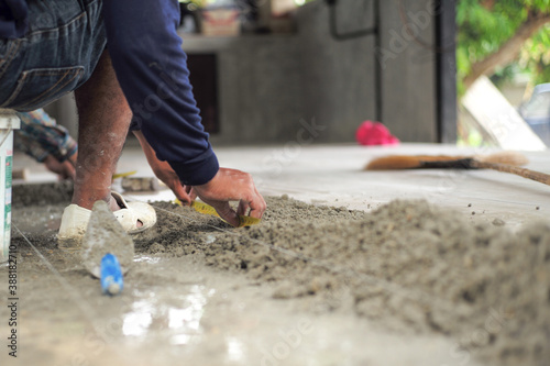 Selective focus on leg and hands of worker mearsuring the floor during installation the floor tiles in the ouse under construction