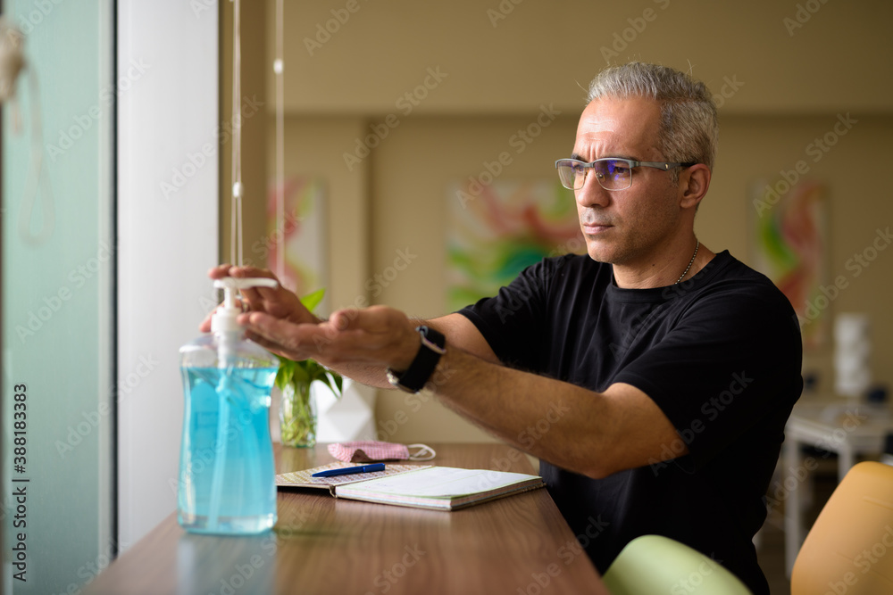 Handsome Persian man with gray hair using hand sanitizer at the library Handsome Persian man with gray hair using hand sanitizer at the library