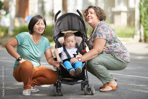 Two cheerful mothers walking in the street with little kid in stroller