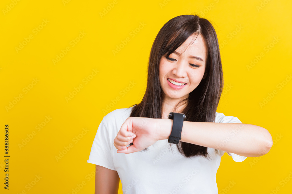 Portrait Asian of a happy beautiful young woman smiling looking and pointing finger her smart wristwatch studio shot isolated on yellow background Portrait Asian of a happy beautiful young woman smiling looking and pointing finger her smart wristwatch studio shot isolated on yellow background