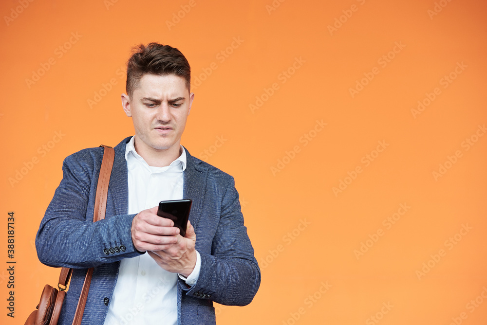 Angry young entrepreneur reading text message from client or colleague, isolated on bright orange Angry young entrepreneur reading text message from client or colleague, isolated on bright orange