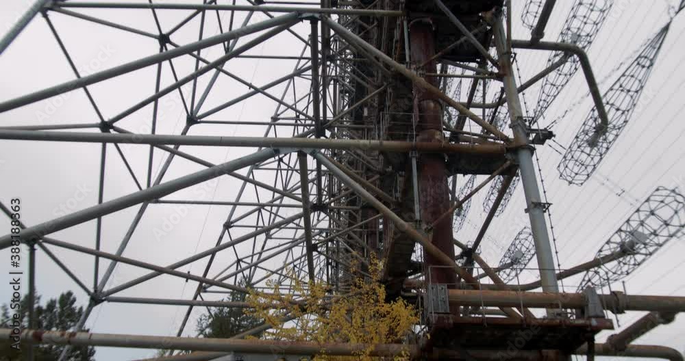 Autumnal Trees Under The Rusty Steel Structure Of Duga Antenna At The Duga Radar Station In Chernobyl Exclusion Zone In Pripyat, Ukraine. - tilt up shot Autumnal Trees Under The Rusty Steel Structure Of Duga Antenna At The Duga Radar Station In Chernobyl Exclusion Zone In Pripyat, Ukraine. - tilt up shot