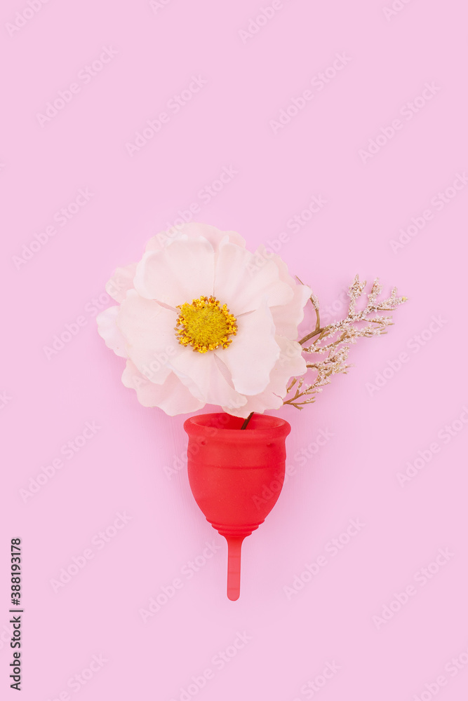 Pink menstrual cup with flowers on light pink background. Feminine hygiene background. Sustainable female care products.