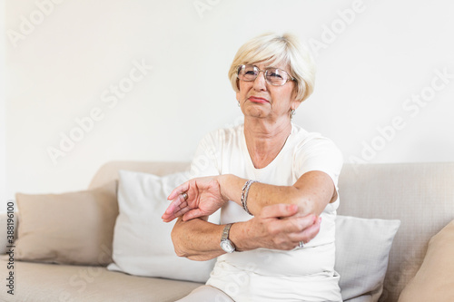 Old age, health problem and people concept - close up of senior woman suffering from pain in hand at home. woman hand holding her elbow suffering from elbow pain. © Graphicroyalty