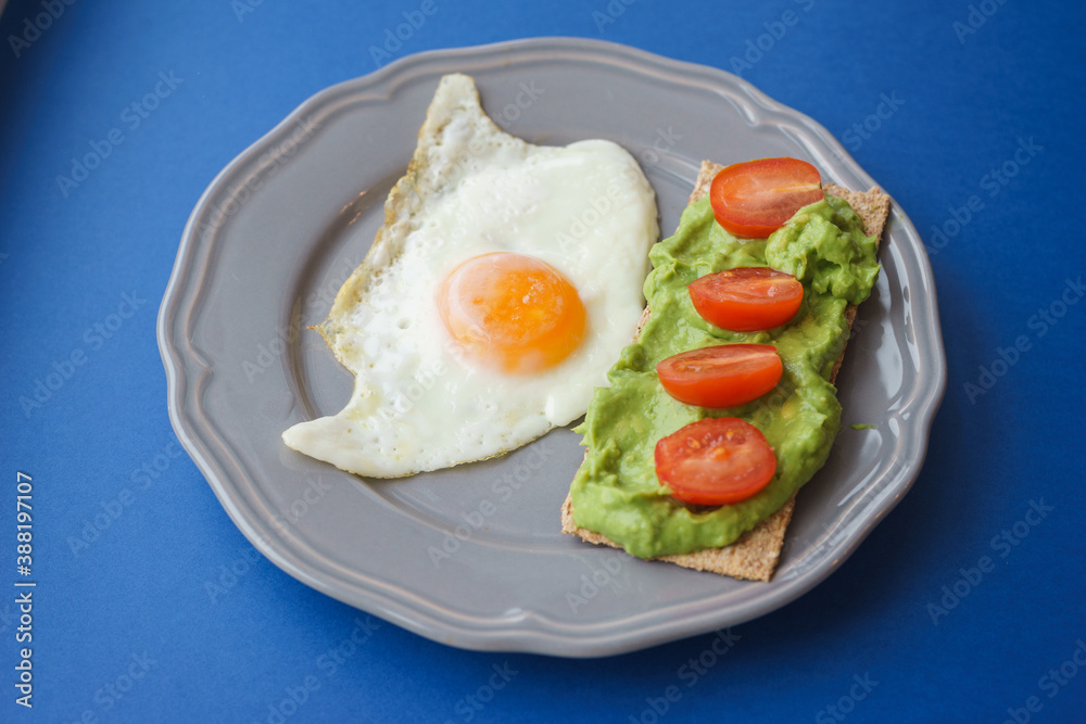 Simple and delicious breakfast: fried eggs on rye bread with guacomole, avocado puree and cherry tomato slices. Simple and delicious breakfast: fried eggs on rye bread with guacomole, avocado puree and cherry tomato slices.